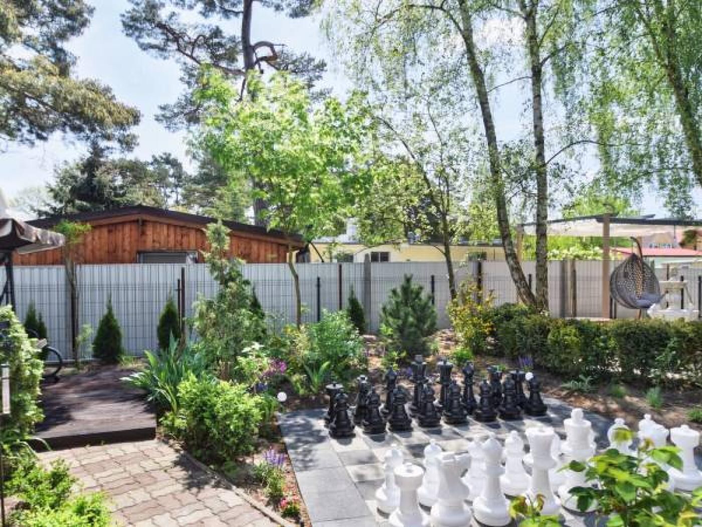 A garden with a chessboard, a wooden shed, and a metal fence.