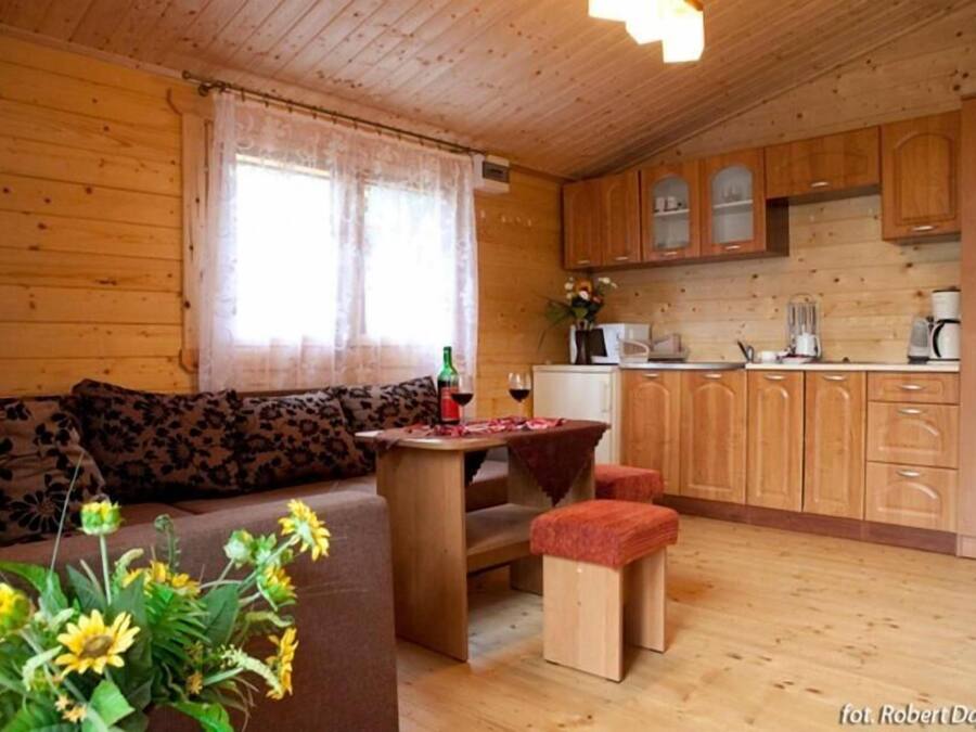 Interior acogedor de una cabaña de madera con sofá, una pequeña mesa de comedor y una zona de cocina con armarios de madera.