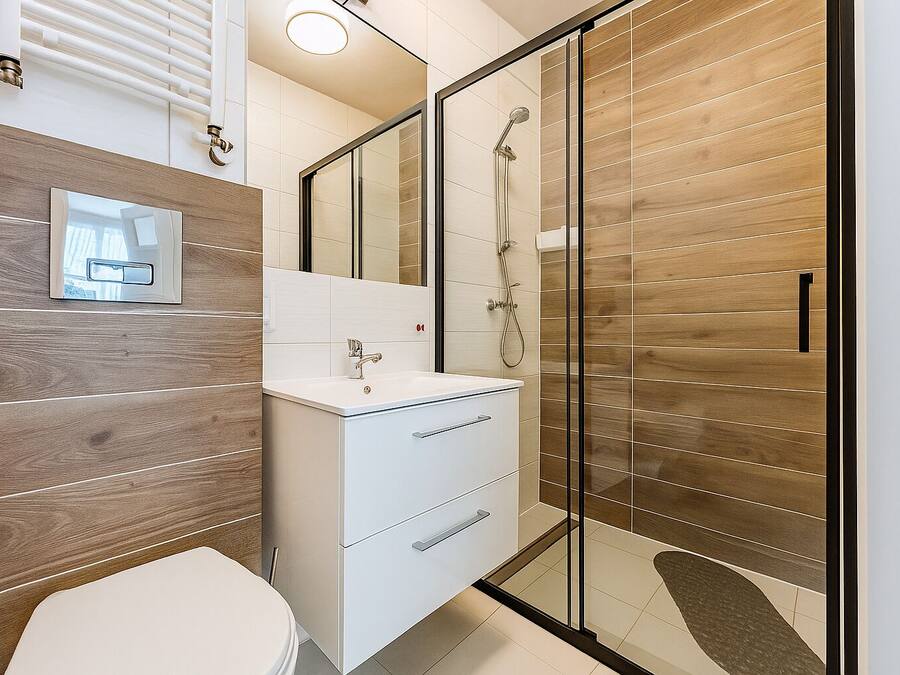 Un baño moderno con cabina de ducha de vidrio, tocador blanco con espejo y panel de pared de madera.