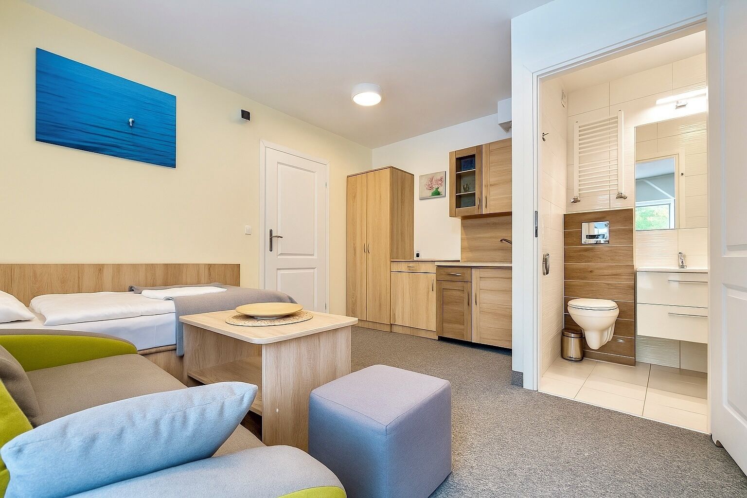 Una habitación de hotel pequeña y funcional con cama, una mesita, sofá y kitchenette.
