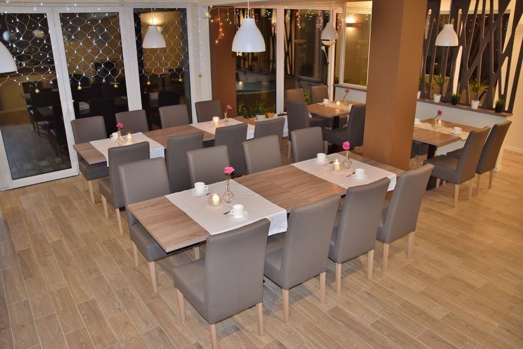 A restaurant with multiple tables and chairs, each with a white tablecloth and candles.