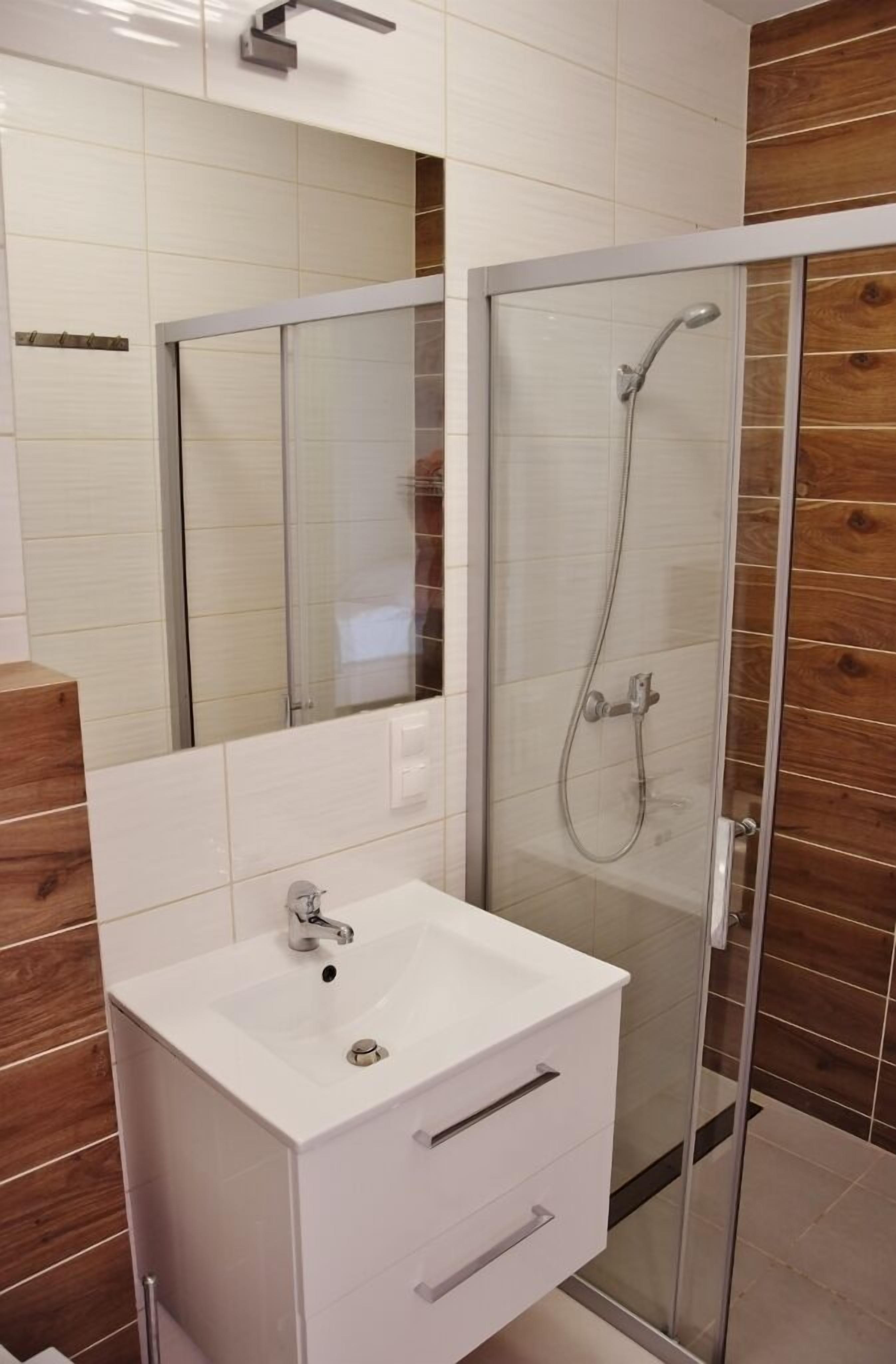 A bathroom with a glass shower enclosure, a white sink, and a wooden panel wall.