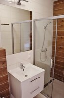 A bathroom with a glass shower enclosure, a white sink, and a wooden panel wall.