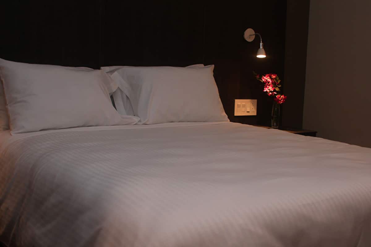 A neatly made bed with white linens in a dimly lit room.