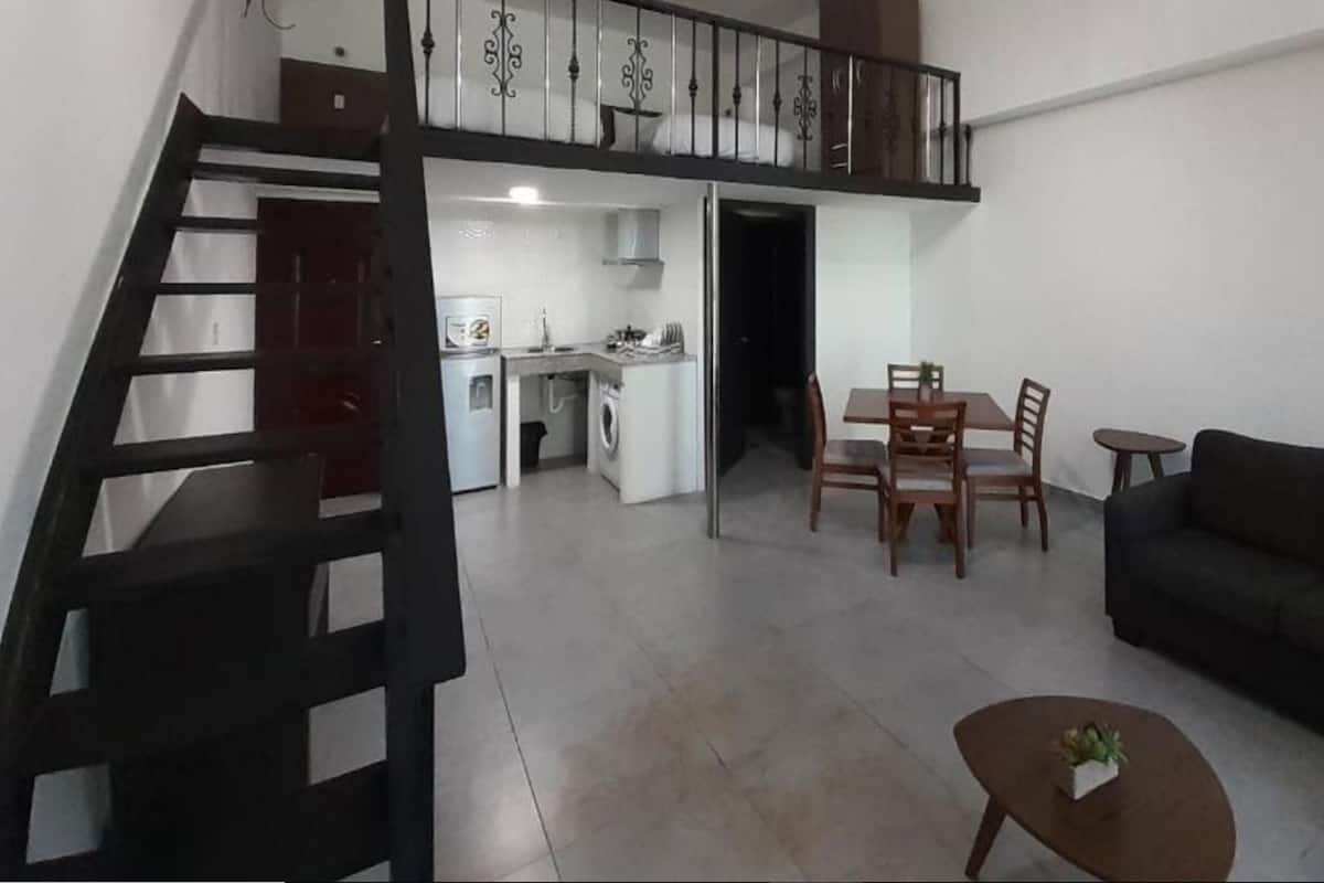 A multi-level apartment with a staircase, a dining area, a sofa, and a small table with a plant.