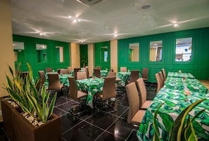 Une salle de conférence aux murs verts, dotée de plusieurs tables et de chaises.