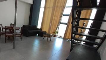 A modern living room with a sectional sofa, a dining table with chairs, and a staircase.