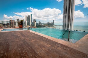 A rooftop pool with a wooden deck, overlooking a city skyline and the ocean. - Innfiniti Hotel & Suites (Panama City)