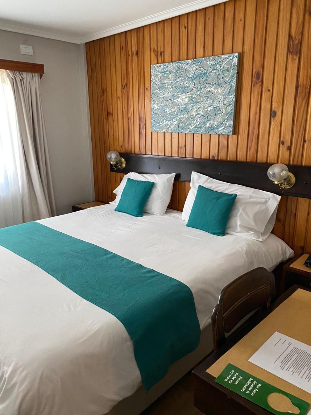 Habitación de hotel con pared de paneles de madera, cama con ropa de cama blanca y turquesa, y un cuadro sobre la cama.