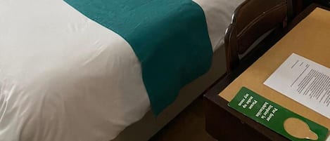Habitación de hotel con pared de paneles de madera, cama con ropa de cama blanca y turquesa, y un cuadro sobre la cama.