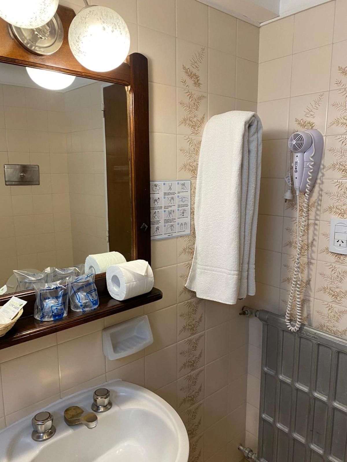 Een badkamer met een wastafel, spiegel, handdoekhouder, haardroger en toiletpapier.