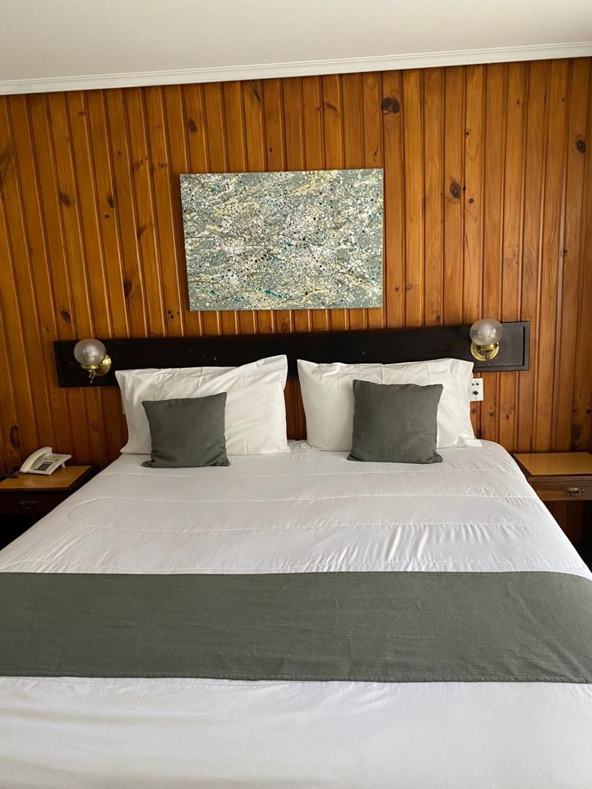 A hotel room with a wooden paneled headboard, a large bed with white bedding, two bedside lamps, and a telephone on the nightstand.
