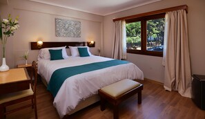 Une chambre à coucher bien rangée, avec un grand lit, un banc en bois, un bureau et un vase rempli de fleurs.