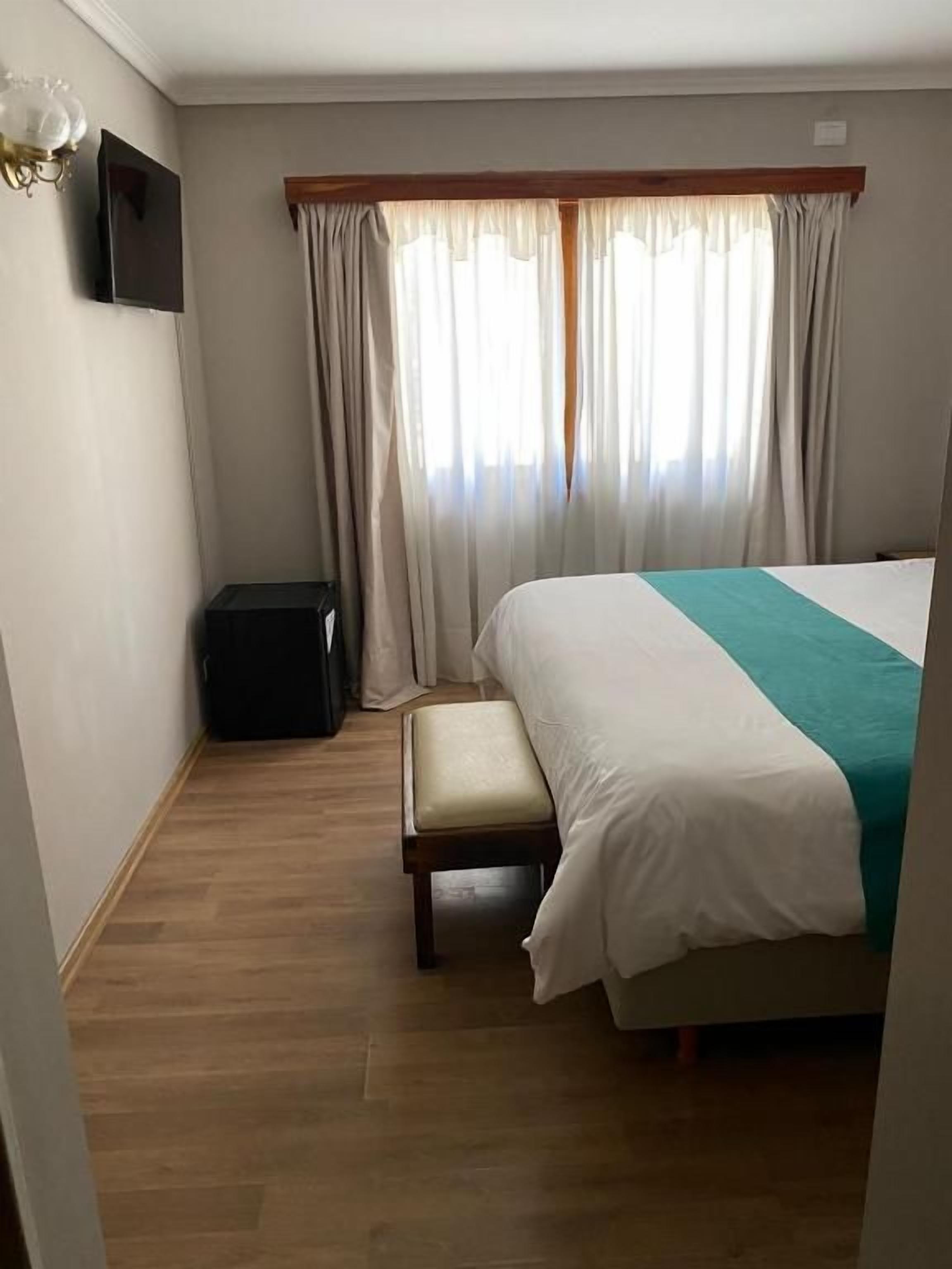Un dormitorio con cama, un banco, televisión y cortinas.