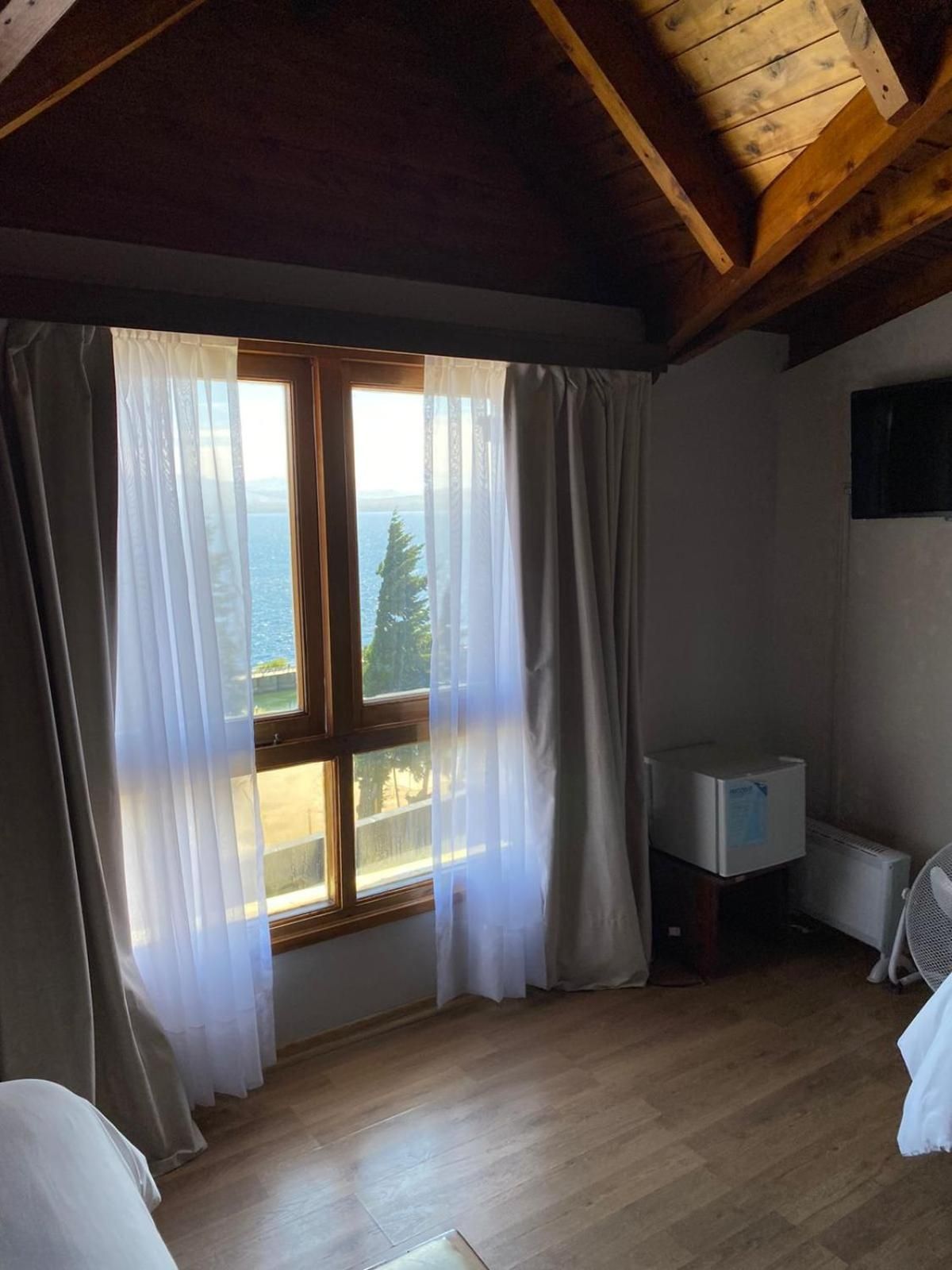 Ein Zimmer mit großem Fenster, Holzboden, einem Bett, einem kleinen weißen Schrank und einem Heizkörper.
