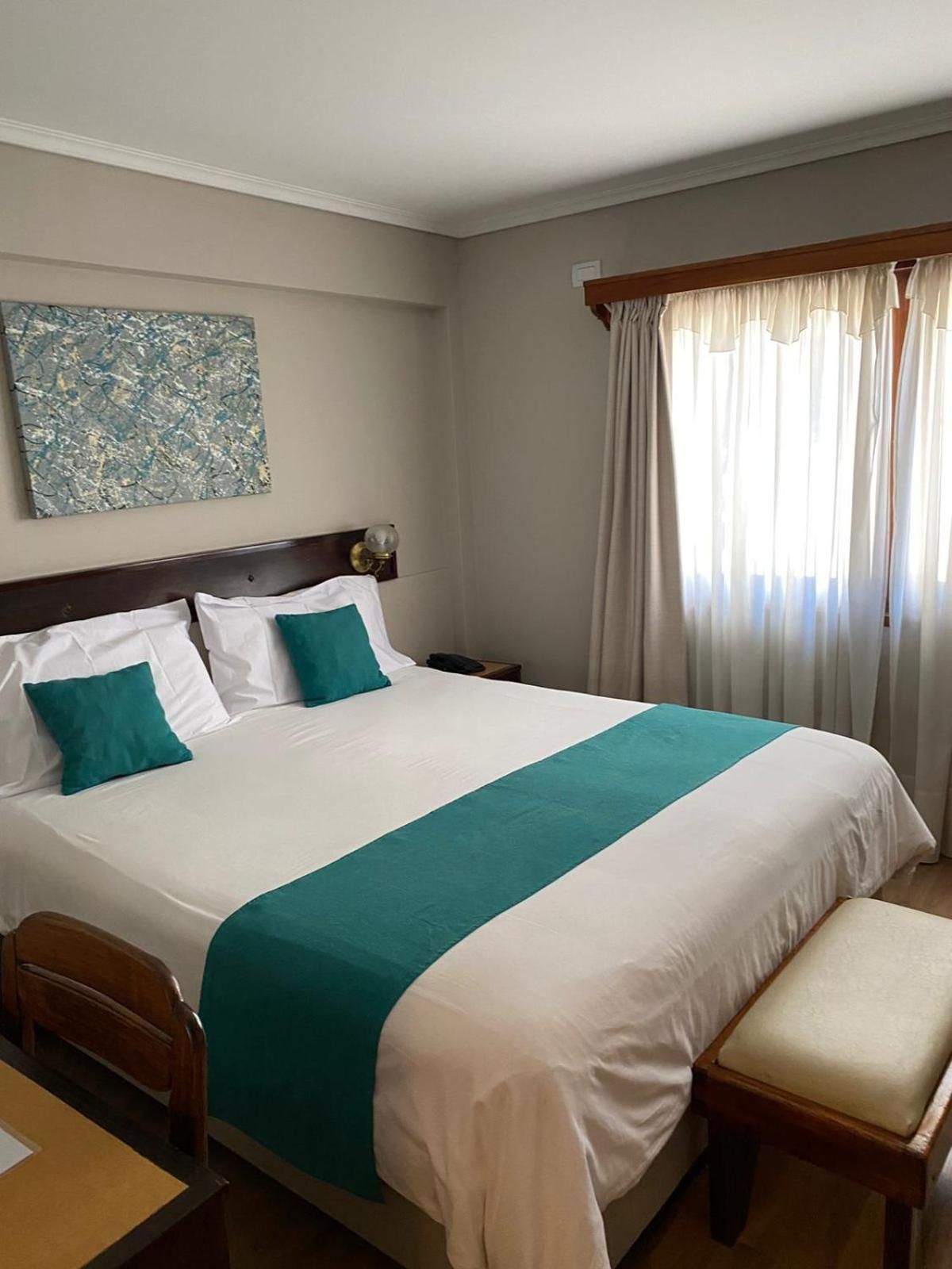 A hotel room with a large bed, a bedside table, a chair, and a window with curtains.