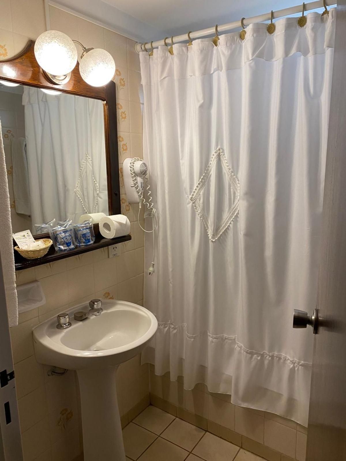 A bathroom with a white sink, a mirror, a hairdryer, and a shower curtain.