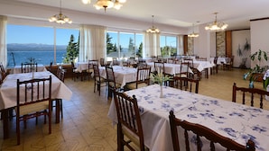 Un comedor con mesas y sillas, ventanas amplias con vista al mar, e iluminación decorativa.