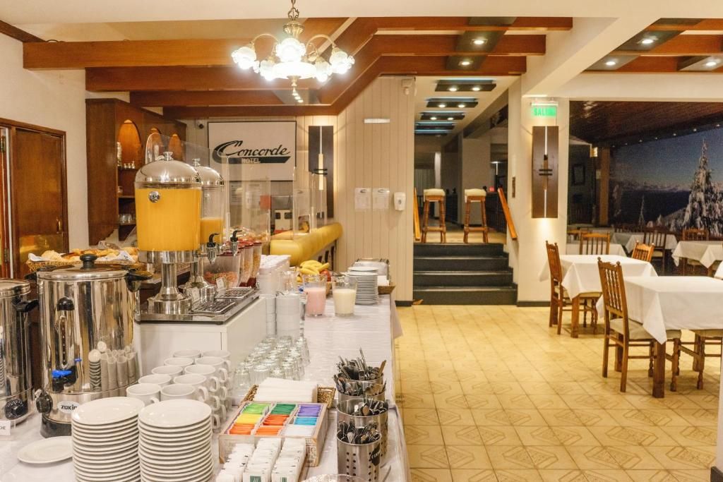 A hotel breakfast area with a buffet setup, including various food items and beverages, and a seating area with tables and chairs.