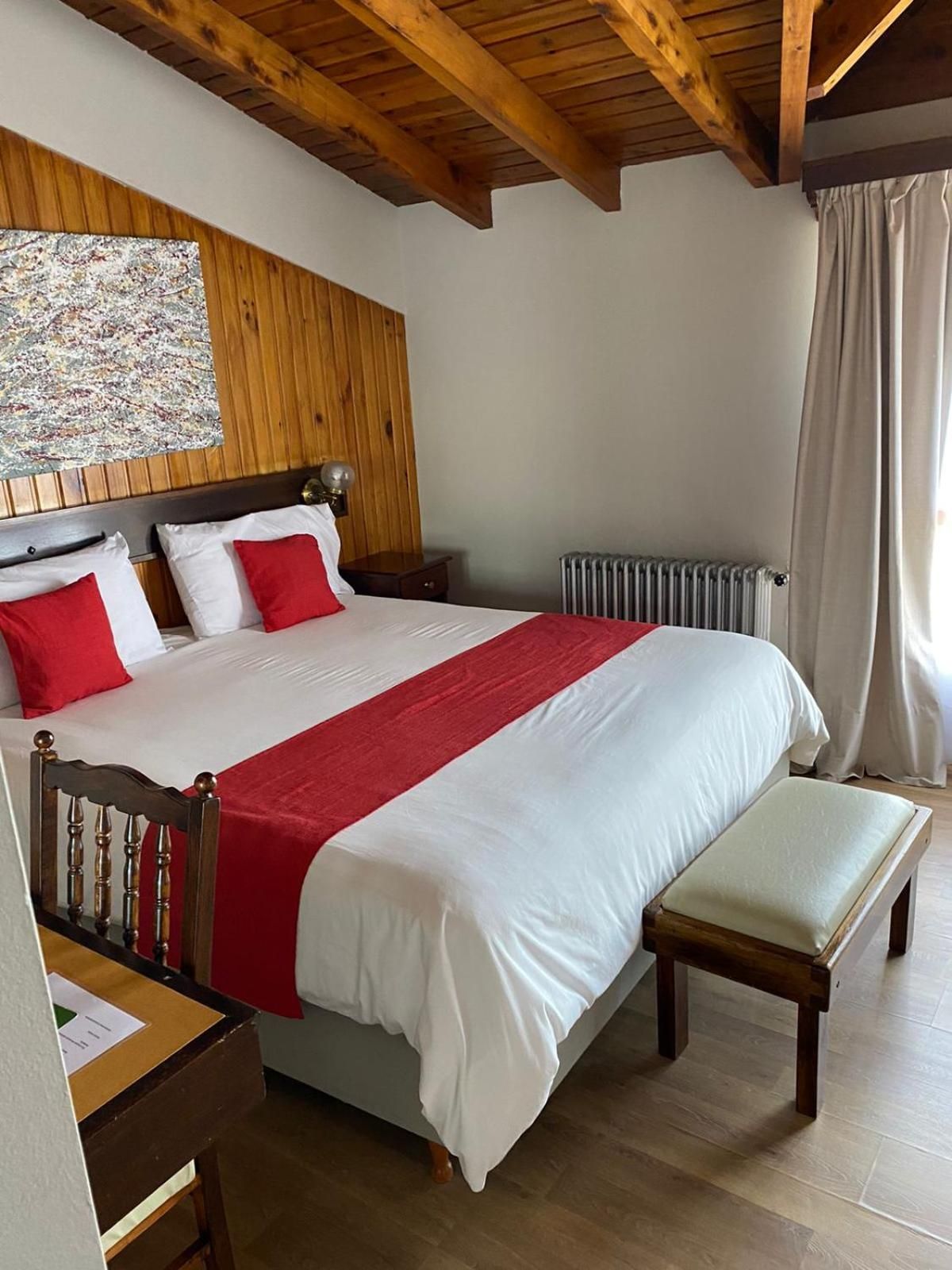 Ein Schlafzimmer mit Holzboden, einem Bett mit weißer Bettwäsche und roten Akzenten, einem Nachttisch, einer Bank und einem Heizkörper.