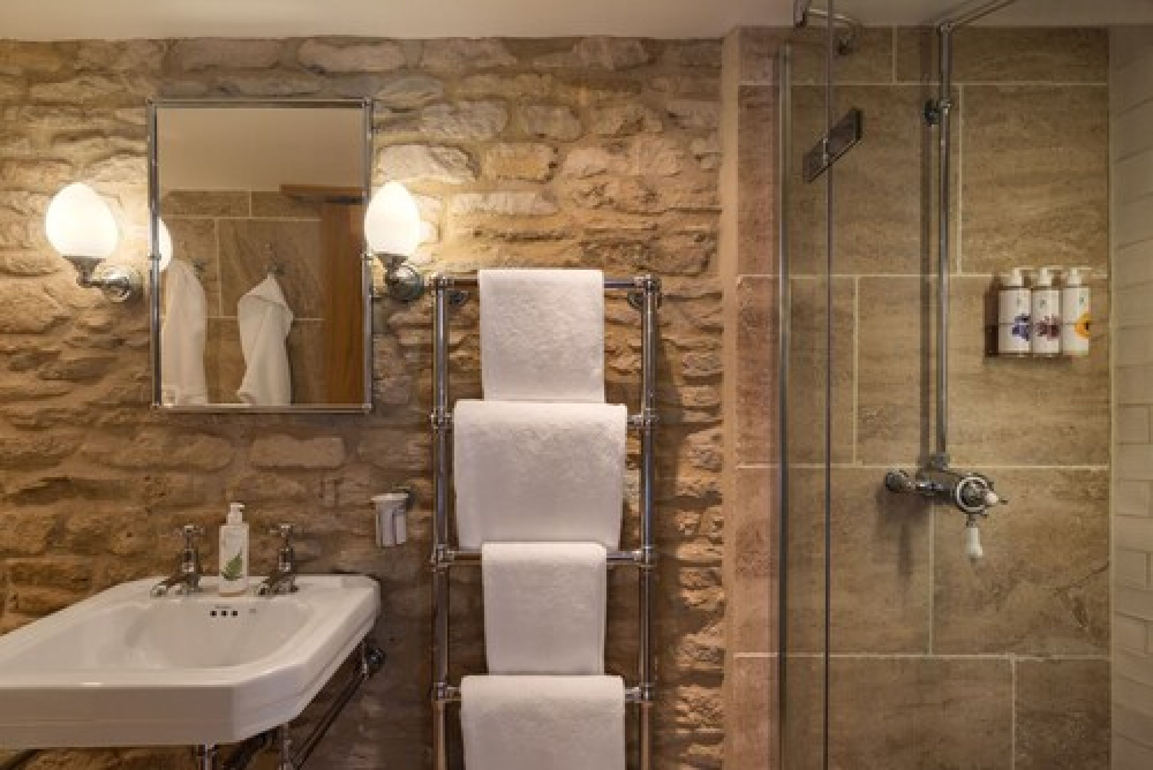 Un baño con pared de piedra, un lavabo con espejo, un perchero y una zona de ducha.
