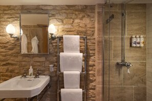 A bathroom with a stone wall, a sink with a mirror, a towel rack, and a shower area. - The Royal Oak Tetbury (Tetbury)