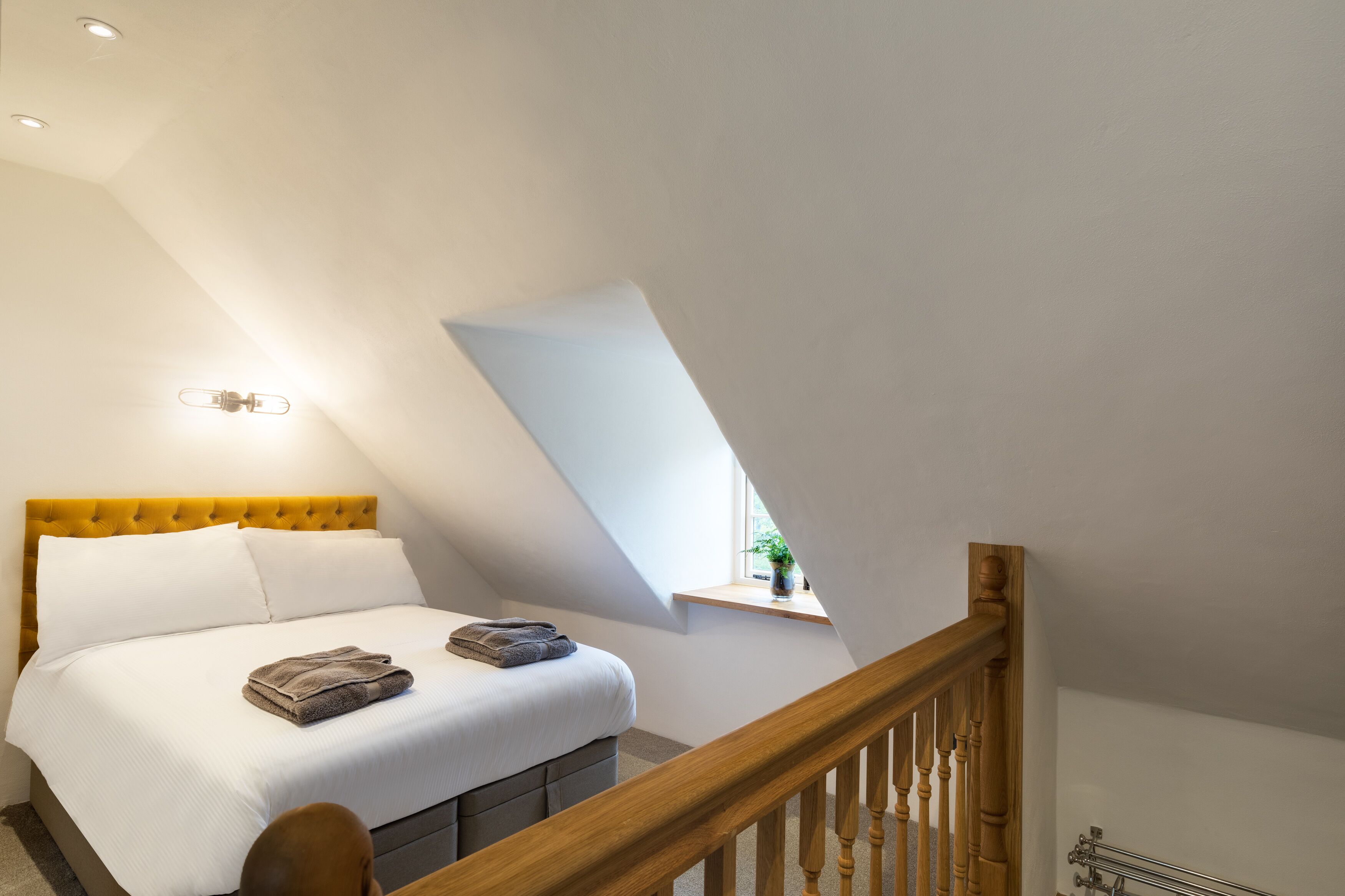 A bedroom with a bed, a window, a wooden staircase, and a ceiling light.