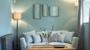 A living room with a sofa, a coffee table, and a lamp. There are three wall-mounted artworks above the sofa.