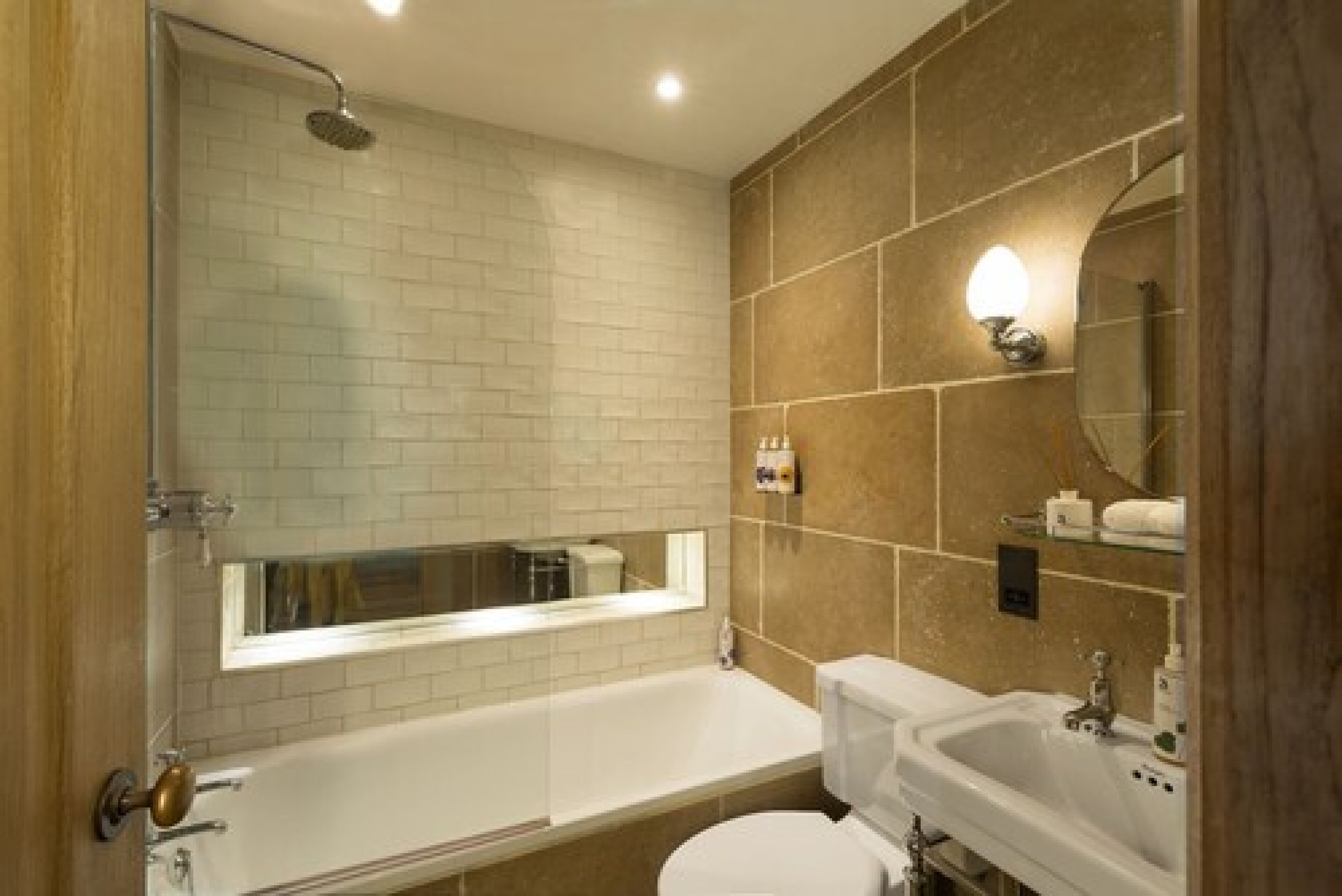 Un baño con bañera, inodoro y lavabo. Hay un espejo sobre el lavabo y un cabezal de ducha sobre la bañera.