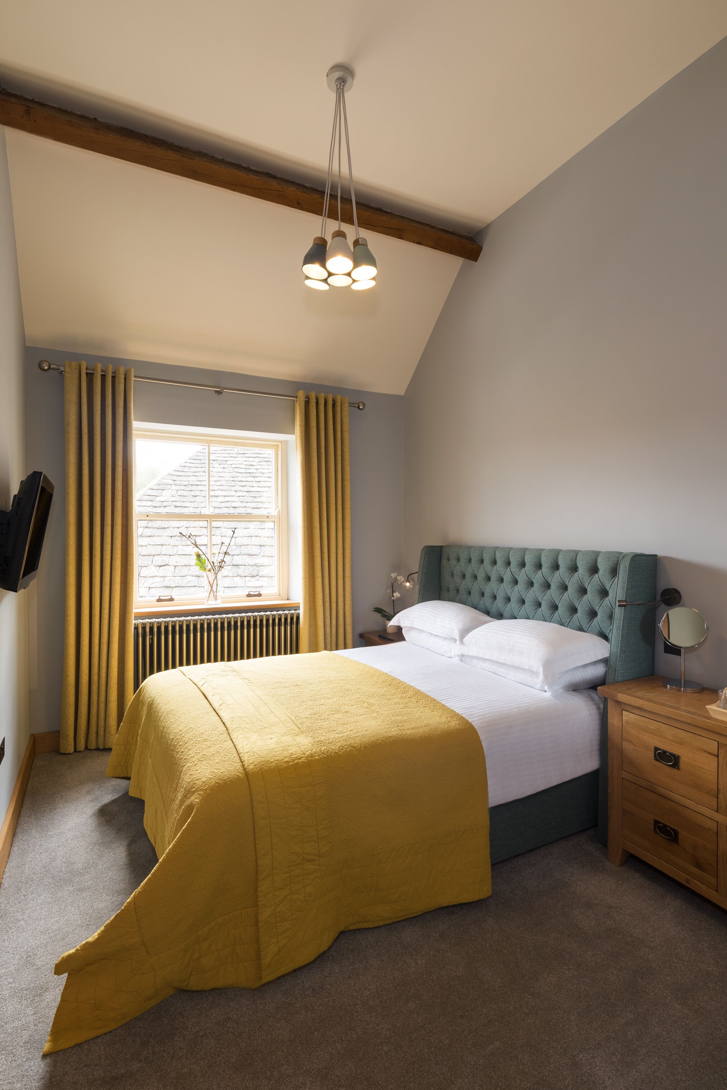 Een slaapkamer met een bed, een raam met gordijnen, een radiator, een nachtkastje met een lamp en een houten nachtkastje.