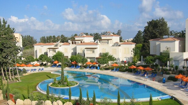 A resort with a central swimming pool, multiple lounge areas with umbrellas, and a landscaped garden. - Villa Hesperides Gardens (Paphos)