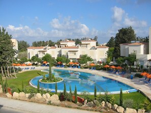 A resort with a central swimming pool, multiple lounge areas with umbrellas, and a landscaped garden. - Villa Hesperides Gardens (Paphos)