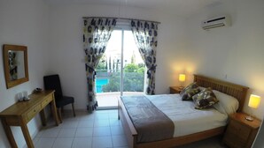 A bedroom with a bed, bedside tables, a desk, a chair, and a balcony with a view. - Villa Hesperides Gardens (Paphos)