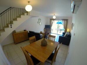 Un área de comedor con una mesa y sillas de madera, un sofá y una escalera.