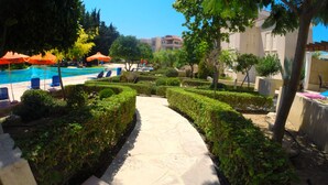 A pool area with a clear pathway, surrounded by neatly trimmed hedges and trees. - Villa Hesperides Gardens (Paphos)