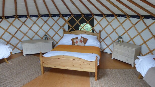 Un lit confortable, avec une structure en bois, se trouve dans une pièce aménagée comme une yourte, avec une simple table de chevet et une petite table.