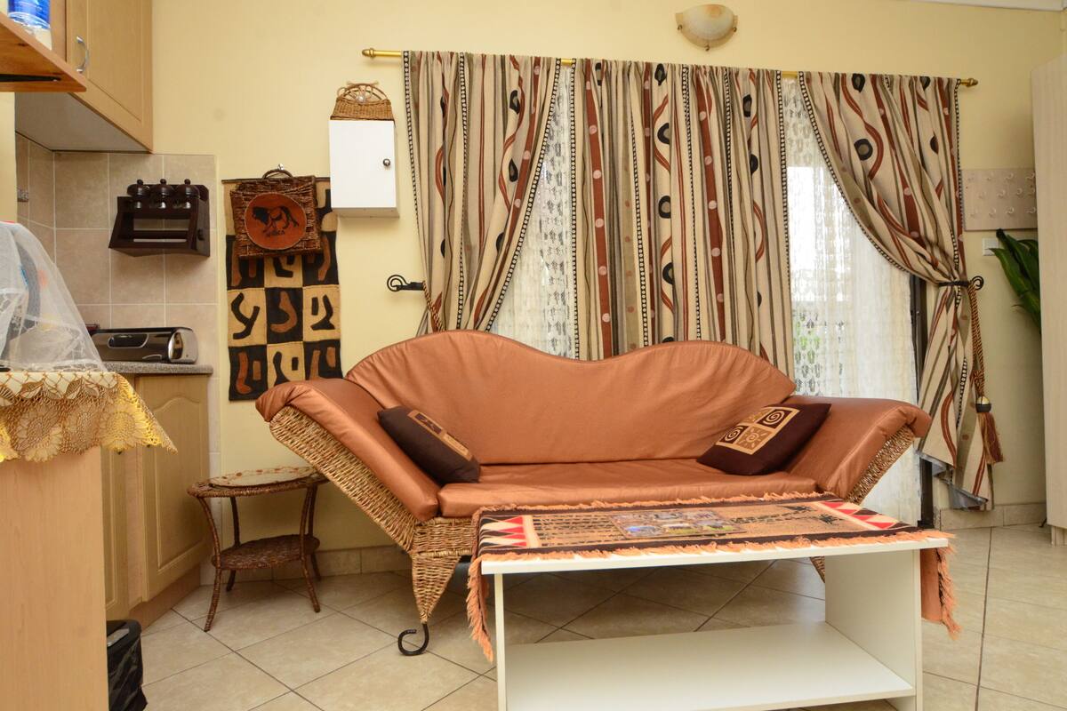 A living room with a sofa, a small table, and a kitchen area with a sink and cabinets.
