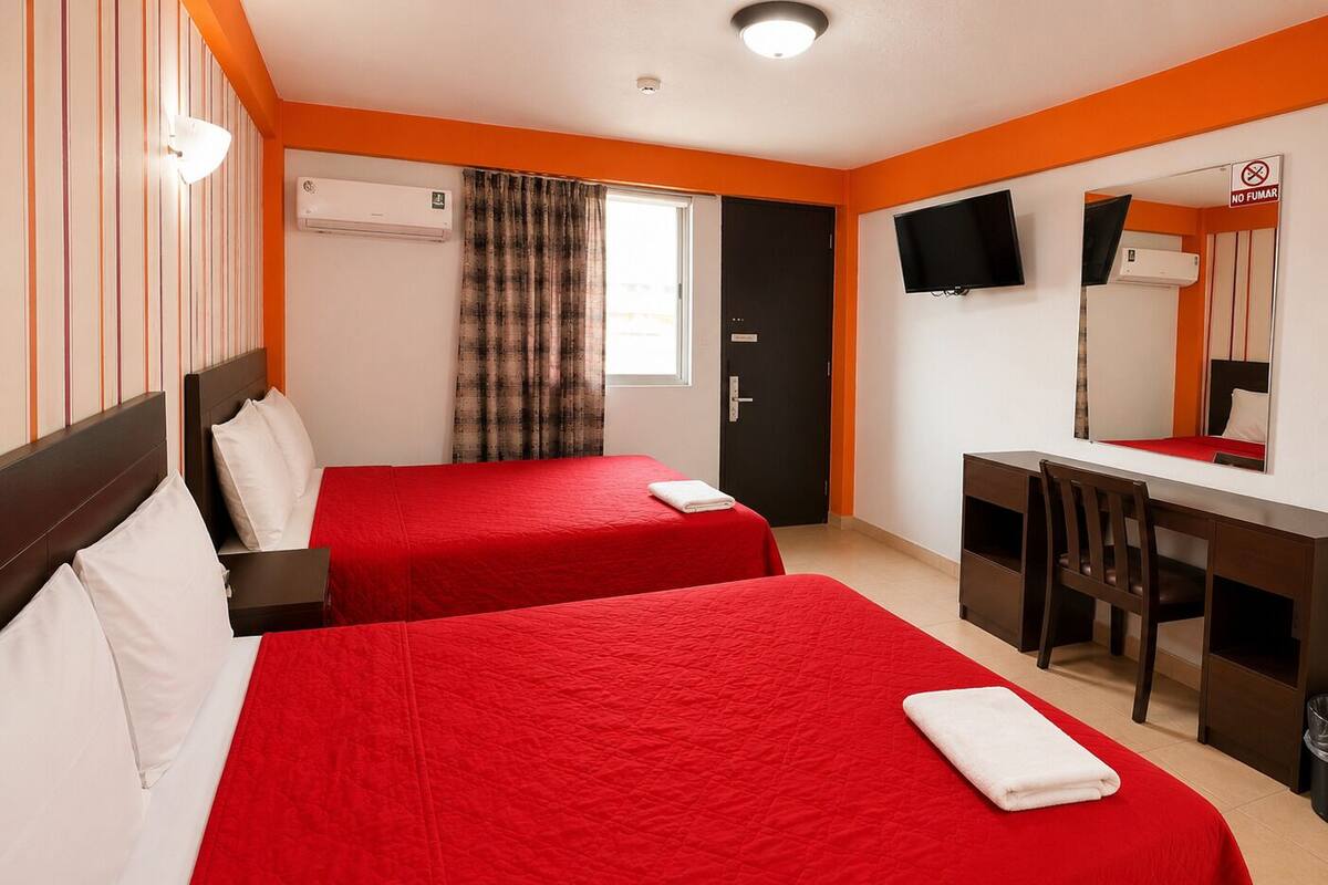Habitación de hotel con dos camas, un escritorio, una silla, un televisor y un cartel de 'NO FUMAR'.