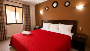 Una habitación de hotel con una cama grande, una mesita de noche, un teléfono y una ventana con cortinas.