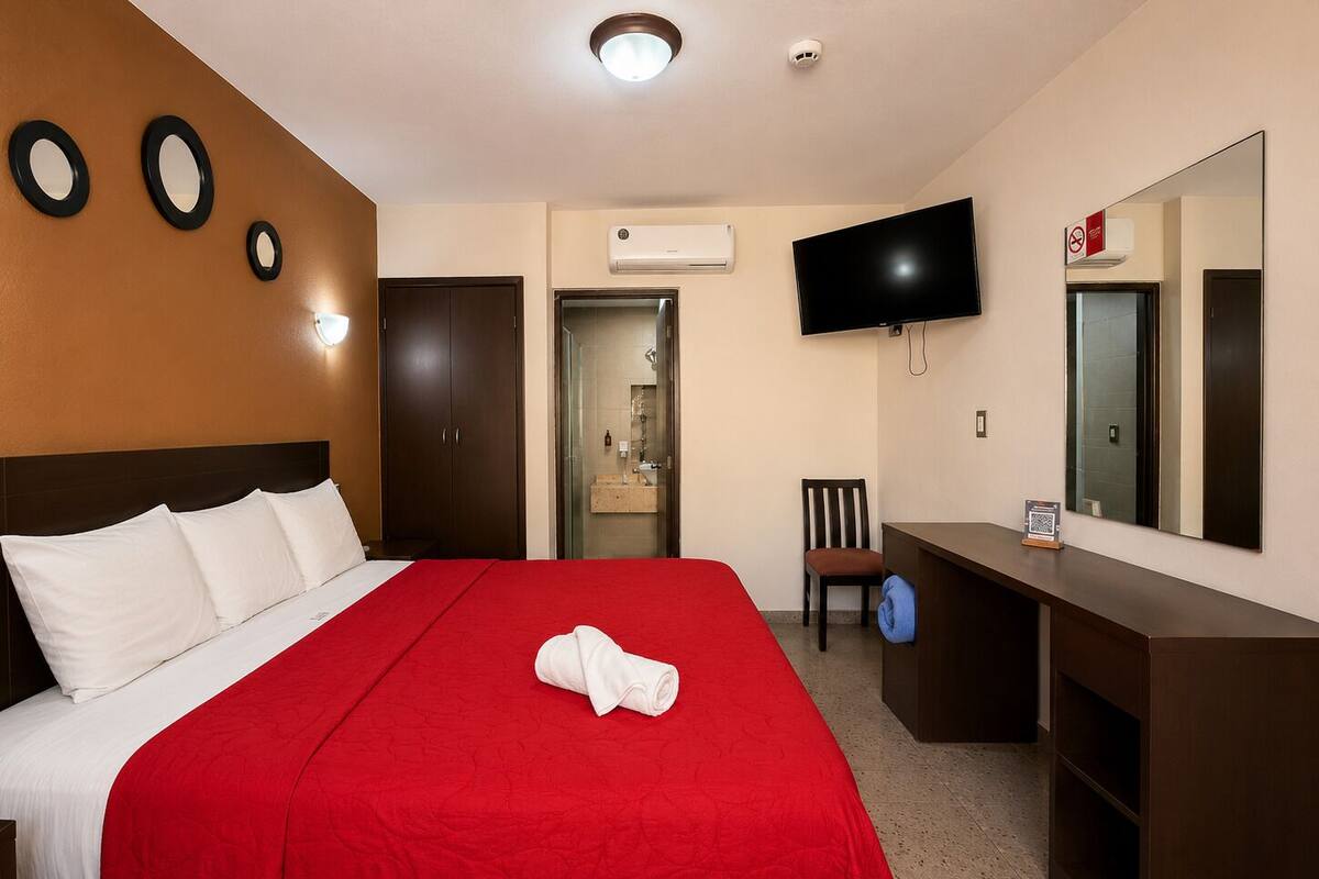 Habitación de hotel con cama, televisor, escritorio y espejo.