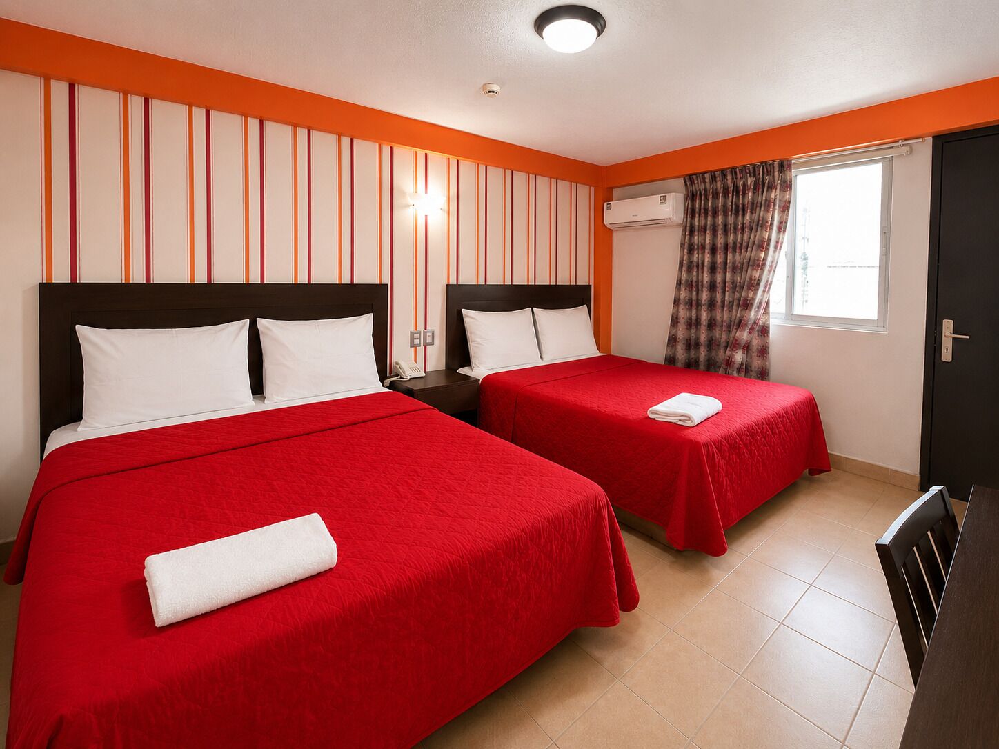 A hotel room with two beds, a window with curtains, an air conditioning unit, and a wall with vertical stripes.