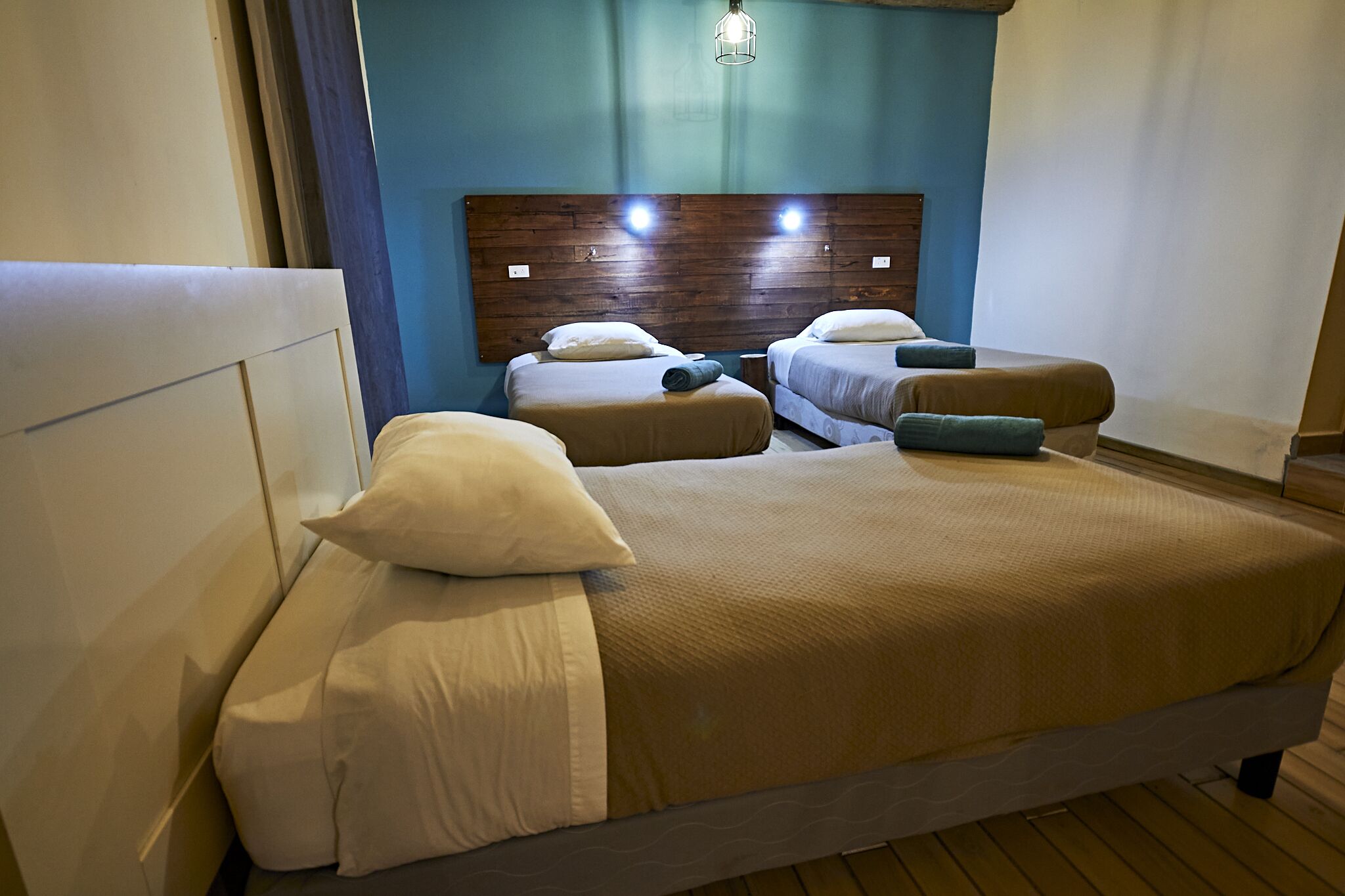 A hotel room with a large bed, two smaller beds, wooden headboard, and a blue accent wall.