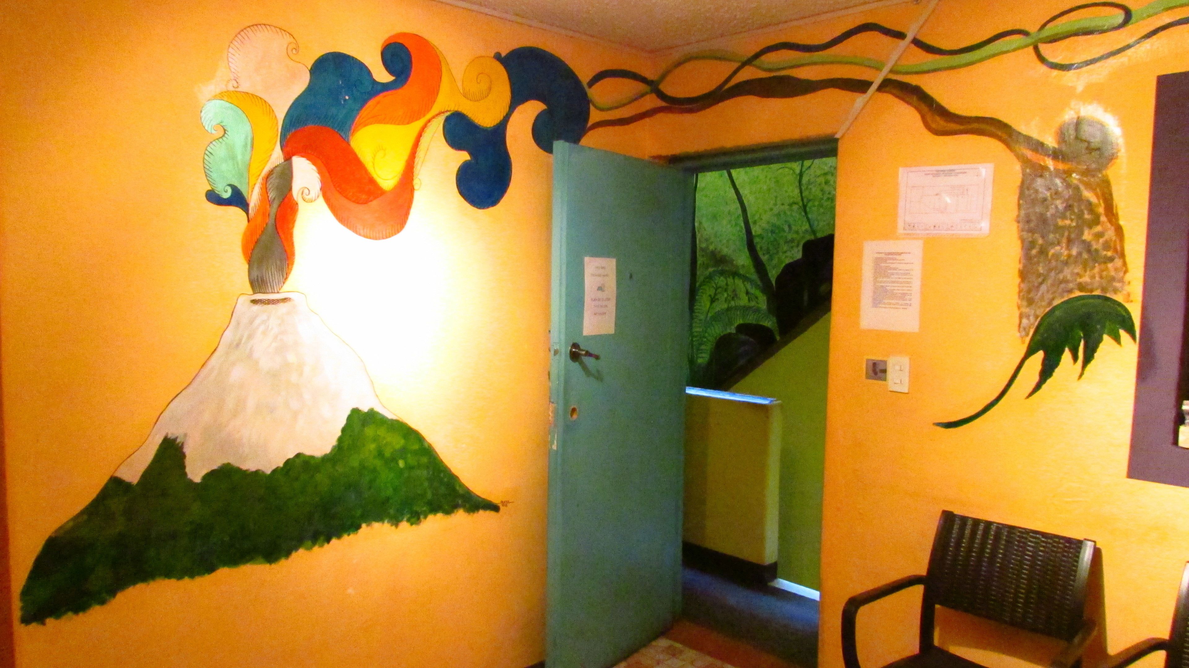 A room with a mural of a volcano, a blue door, a chair, and a green wall.