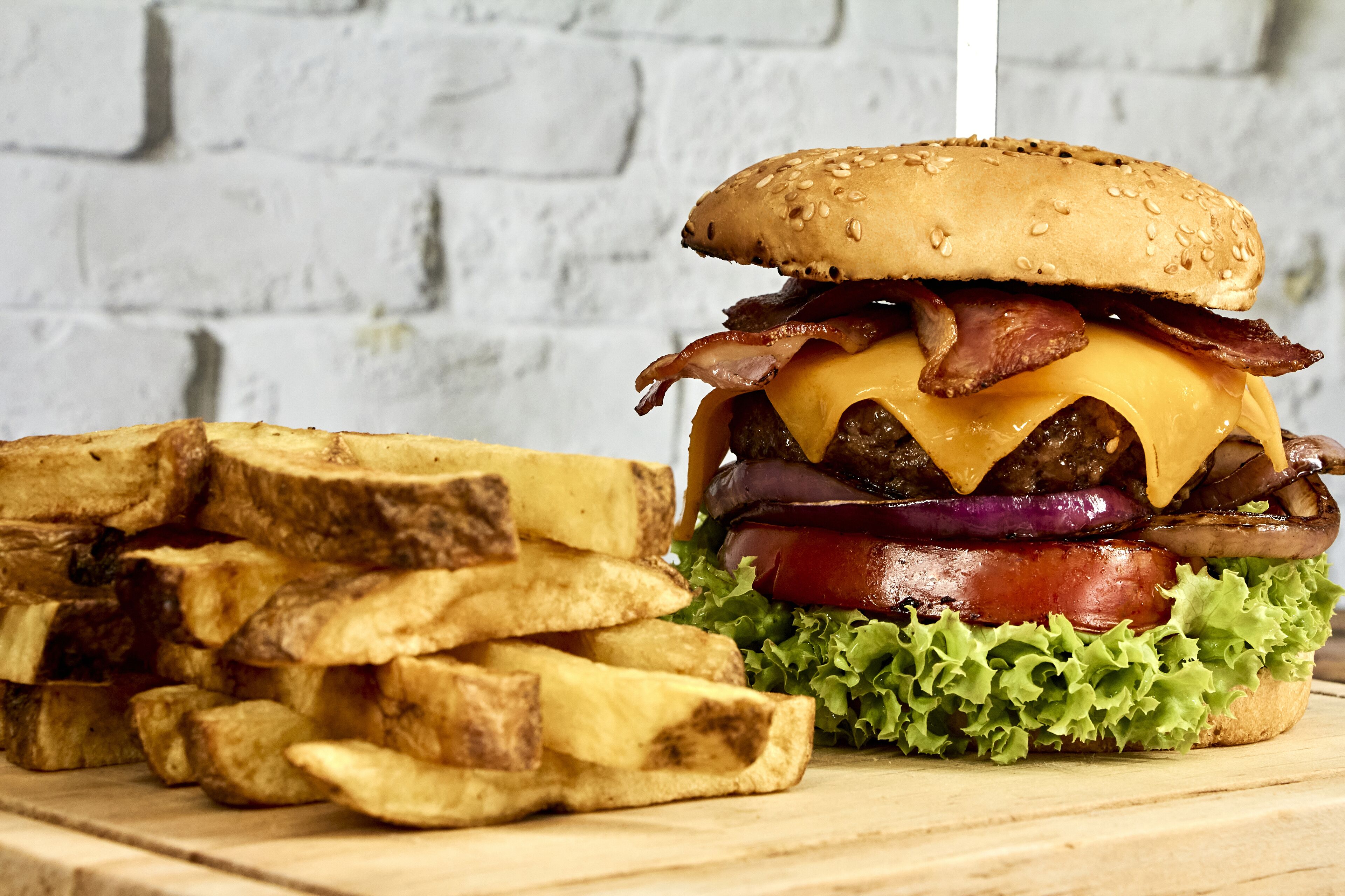 En hamburgare med sallad, ost, bacon och ett sesamfröbröd, serverad med en stor portion pommes frites.