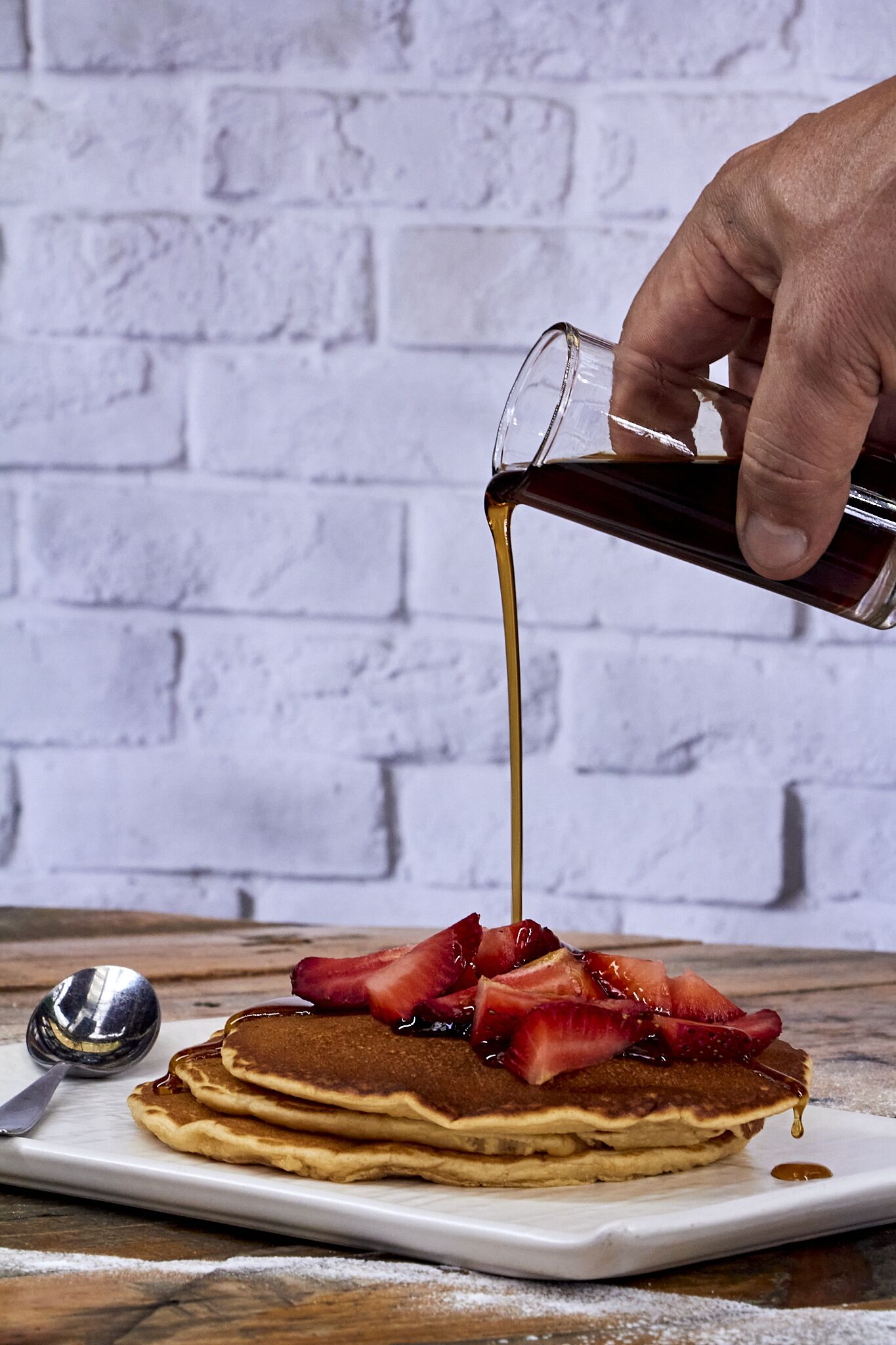 A stack of pancakes with syrup and strawberries on a white plate.