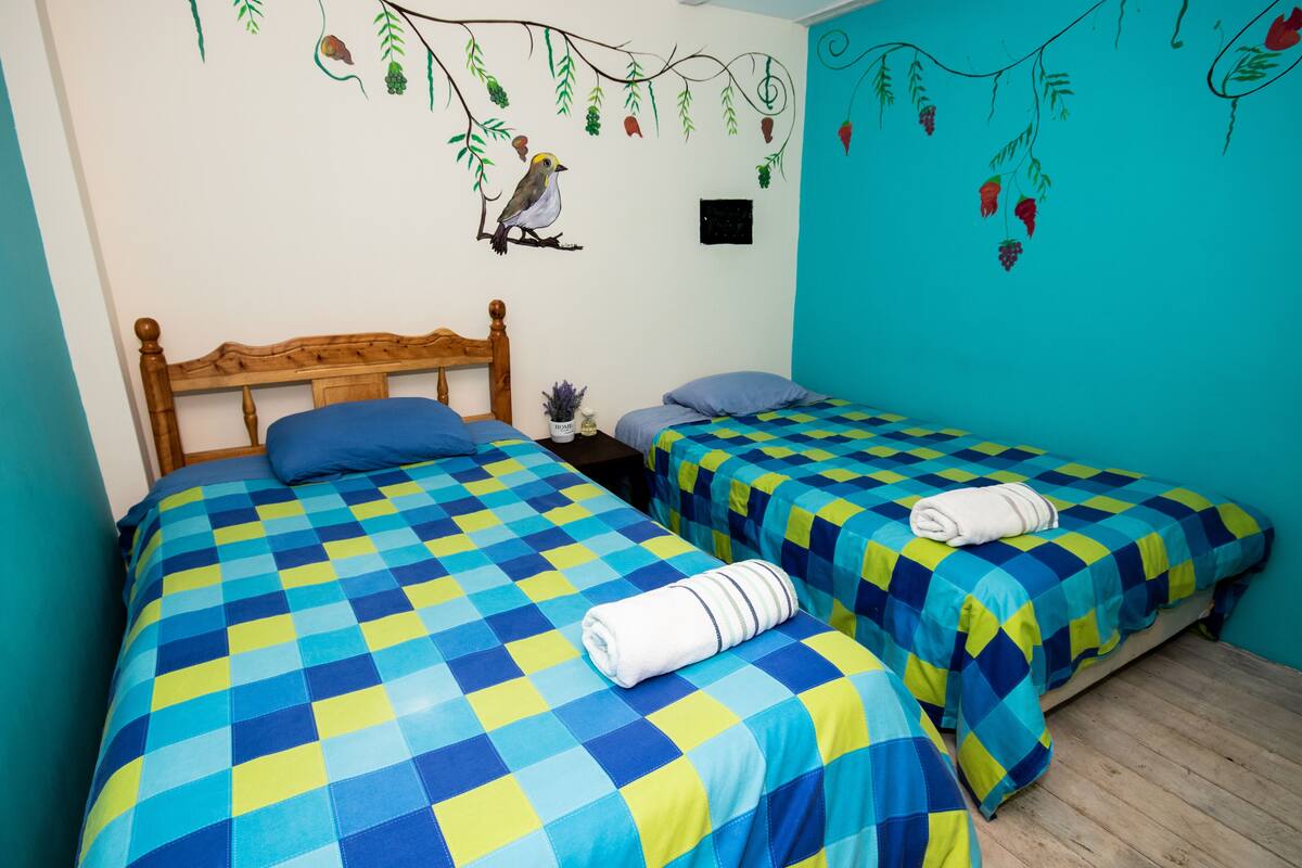 A bedroom with two beds, each with a blue and yellow checkered bedspread and a rolled towel on one bed.