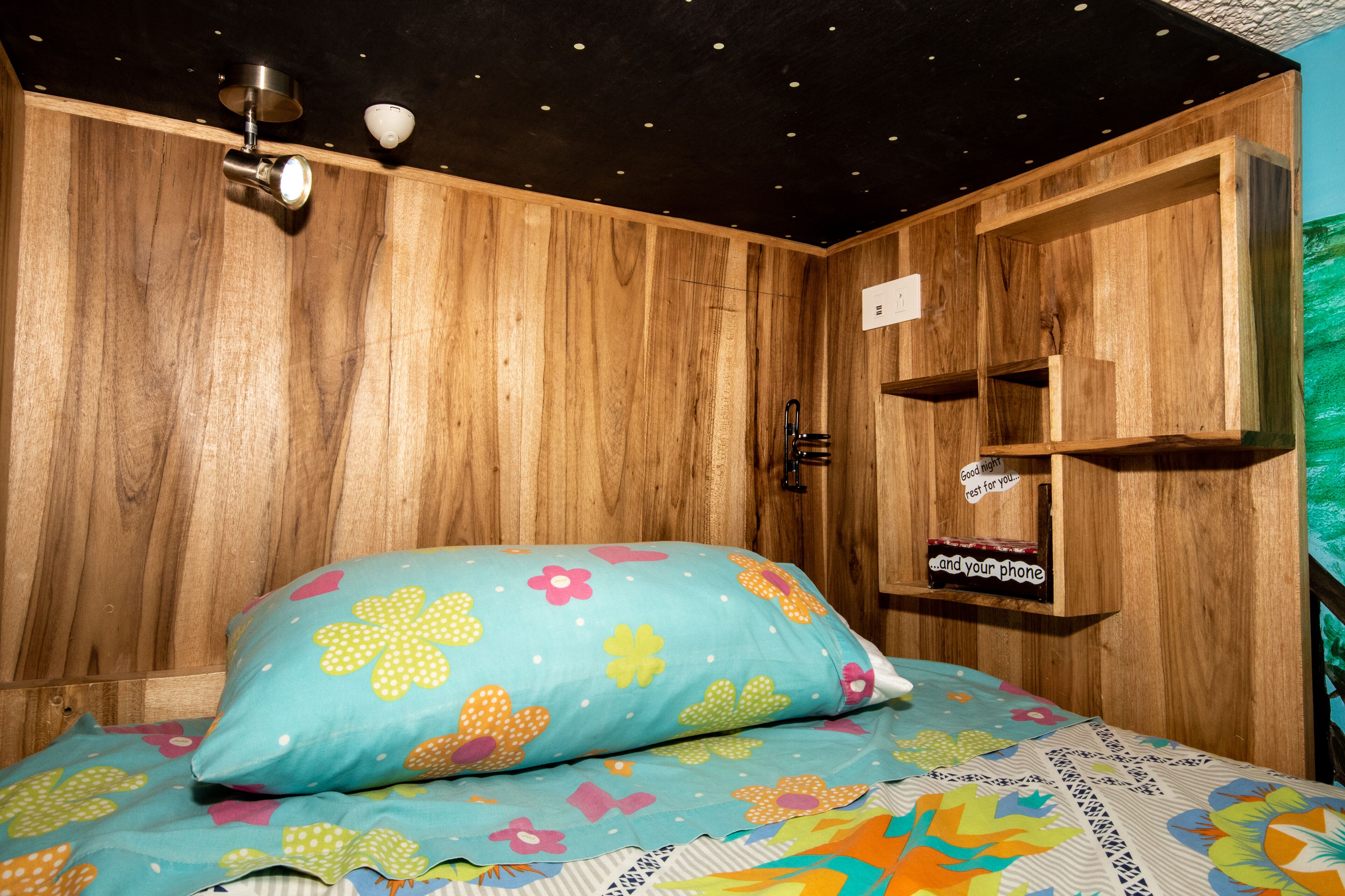 Una habitación de madera con una cama, un estante con un cartel y un techo con luces.