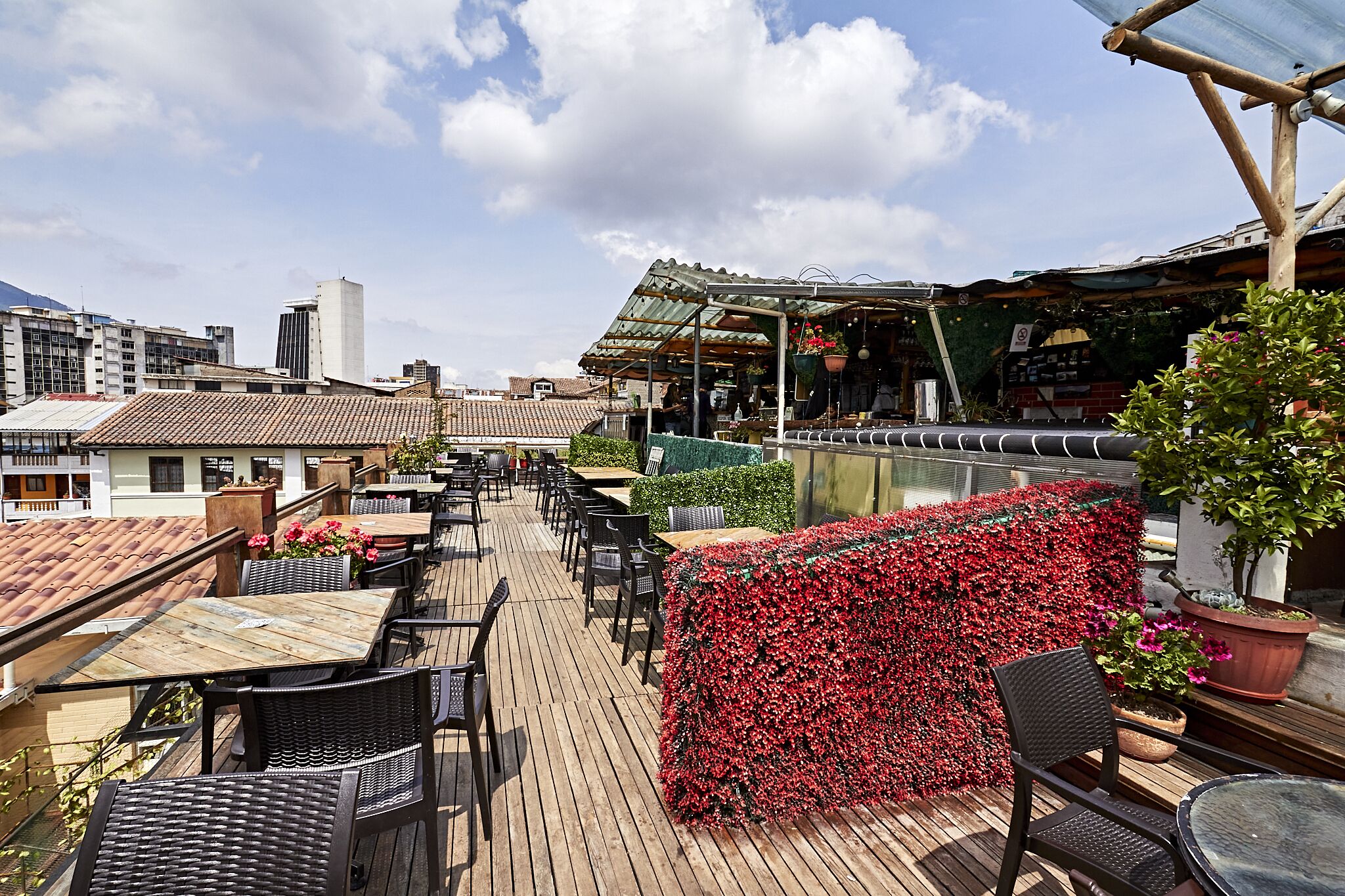 Un espace extérieur aménagé avec des tables et des chaises, une terrasse en bois et une vue sur le paysage urbain en arrière-plan.