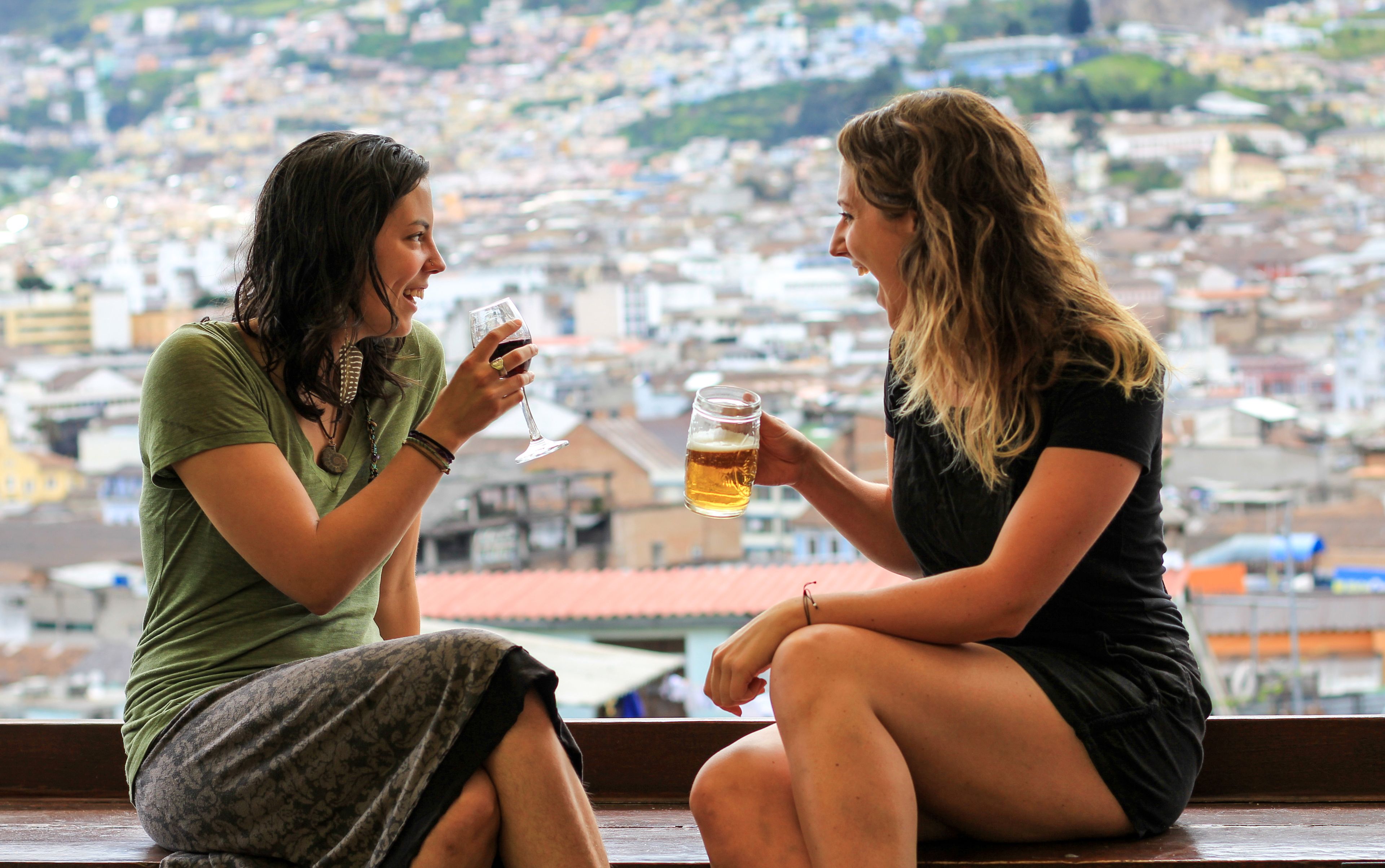 Two individuals sitting on a bench with a cityscape view in the background.
