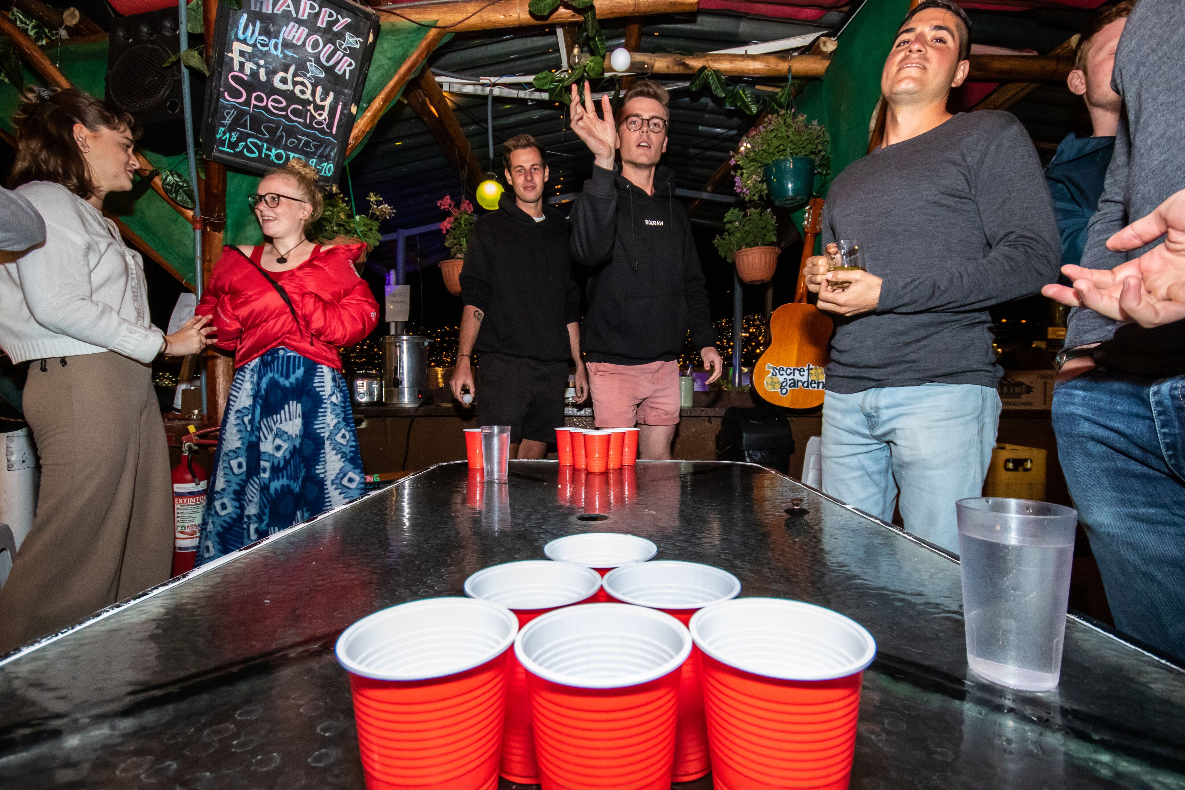 A group of people around a table with red plastic cups, some holding drinks.